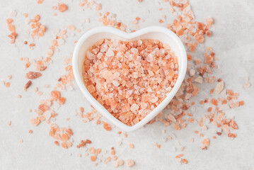 Pink Himalayan coarse crystalline salt in the heart shape  white bowl and scattered on a light textured background top view