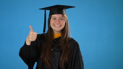 Portrait of graduate girl with diploma, shows gesture of victory and success on blue background, celebrating graduation from the high school or University, excited dancing party