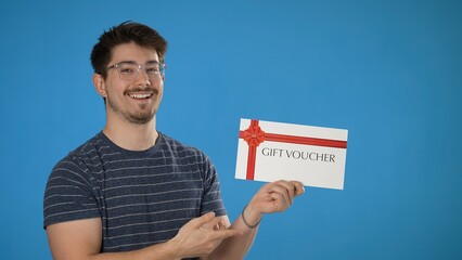 Portrait of smiling happy handsome young man striped t-shirt holding gift certificate voucher coupon isolated on blue background in studio.