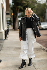 full length of blonde woman in leather shirt jacket and cargo pants walking on urban street in Miami.