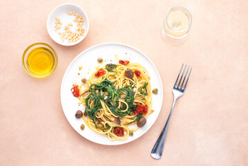 Spaghetti  with Italian Agretti, Barba di frate or Saltwort or  Salsola Soda, olives, anchovy, tomatoes, capers,  pine nuts and olive oil, spring Italian recipes. Pink soft spring background