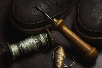 Tailoring and shoe repair. Shoes and an awl with threads on a wooden table