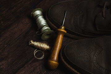 Tailoring and shoe repair. Shoes and an awl with threads on a wooden table