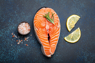 Fresh raw salmon fillet steak with rosemary on dark blue rustic stone background with rose salt and lemon top view, healthy balanced diet and nutrition with fish