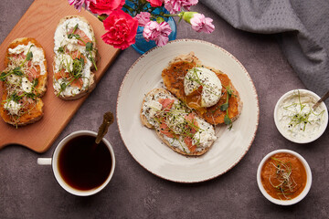 Morning food - sandwiches with poached egg, salmon, zucchini, greens and cream cheese spread, cream and zucchini sauce, coffee cup flat lay.