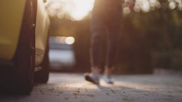 Unrecognizable man getting ready to seat in a convertible car and drive. Male approaches the car, opens the door and gets inside preparing to ride on a summer sunny evening at sunset.   