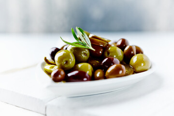 Green and Kalamata olives with fresh rosemary on bright wooden background. Close up. 