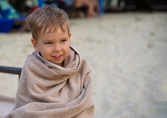 The baby, wrapped in a towel, is warming himself on a sun lounger by the sea. Baby in anticipation of bathing