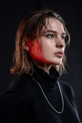 A slender, beautiful young girl in black clothes poses in a neon red-blue light on a black background.Black on black. Neon
