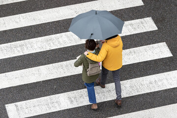 Scene of a couple walking together with an umbrella on a city zebra crossing on a rainy day