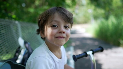 One cute little boy seated at park bench outside. Portrait of a child resting outdoors during beautiful sunny day