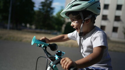 Naklejka premium One active little boy riding bicycle outside. Happy child learning to ride bike wearing helmet outdoors. Childhood development growth concept