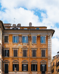 Photograph of an old yellow building in the city of Rome. The image shows only the building and the sky with some clouds in the background, creating a serene and quiet atmosphere.