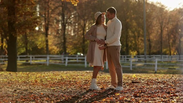 Pregnancy , motherhood and parenthood concept. Happy pregnant woman and man hugging, touching belly and listening baby's kicks and walking outdoors in autumn park. Family is expecting for unborn baby.