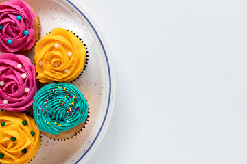 Cupcakes with cream icing on plate on white background, top view with copy space