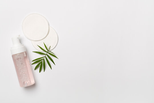 Foaming facial cleanser and with eco pads on color background, top view