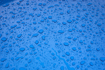 Closeup of rain drops on blue car by rainy day