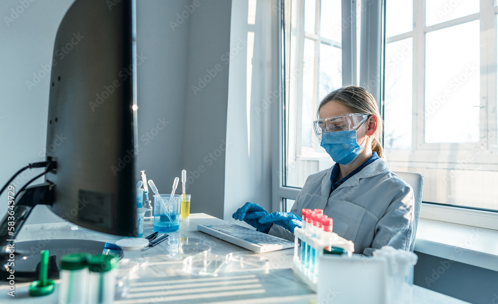 Poster a female researcher sits at a workplace in a laboratory, behind a personal computer monitor. against