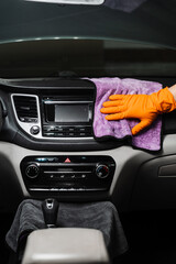 Worker in an auto detailing service is using microfiber cloth to manually dry the interior of car,...