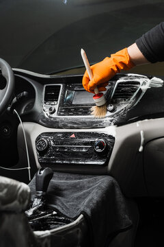 Cleaning with brush and detergent of air dashboard and multimedia in the car. Worker in detailing auto service clean elements of interior of car.