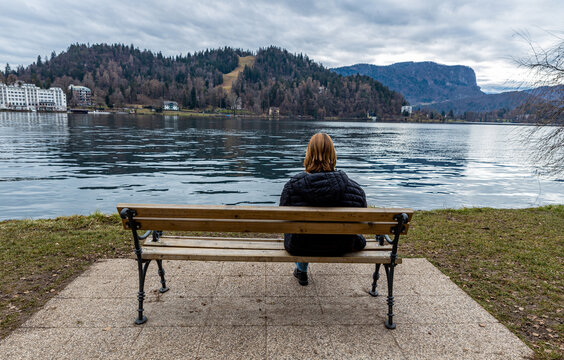 A girl sitting alone on a bench on the shore of the Slovenian Lake Bled in winter