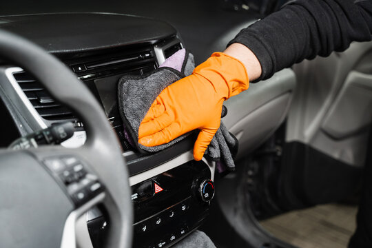 Worker cleans cars using microfiber cloth to dry the dashboard during the process of hand-drying the interior of the car in detailing service.