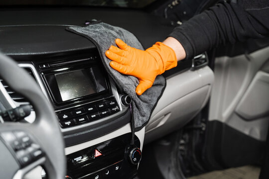 Worker cleans cars using microfiber cloth to dry the dashboard during the process of hand-drying the interior of the car in detailing service.