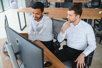 Two successful trader sitting in office and looking at screen, checking cryptocurrency information data on finance market graph, pointing on monitor