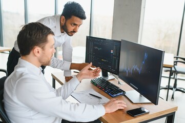 Fototapeta na wymiar Two successful trader sitting in office and looking at screen, checking cryptocurrency information data on finance market graph, pointing on monitor