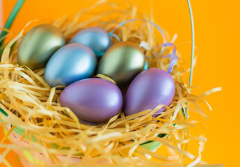 Multi-colored Easter eggs in a nest, Easter in a basket on a festive orange background. The minimal concept of Easter. Easter card with a copy space for text.
