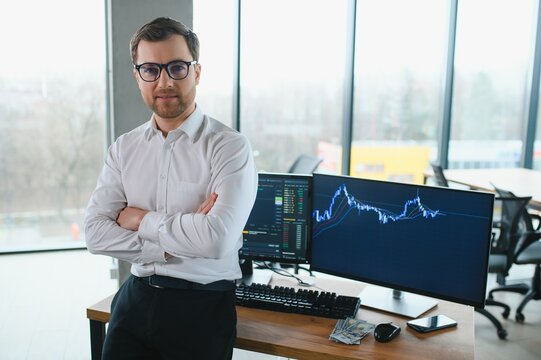 Man trader in formalwear sitting at desk in frot of monitors with charts and data at office browsing laptop checking documents analyzing stocks price changes concentrated.