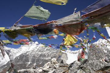 En primer plano piedras con banderas de plegaria de colores budistas ondeando al viento y de fondo...