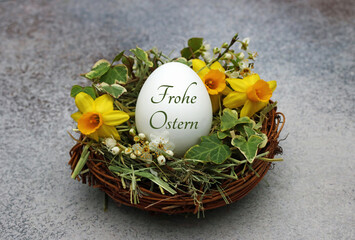 Dekoratives Osternest mit Narzissen, Efeu und einem beschriftetem Osterei mit dem Text Frohe Ostern.