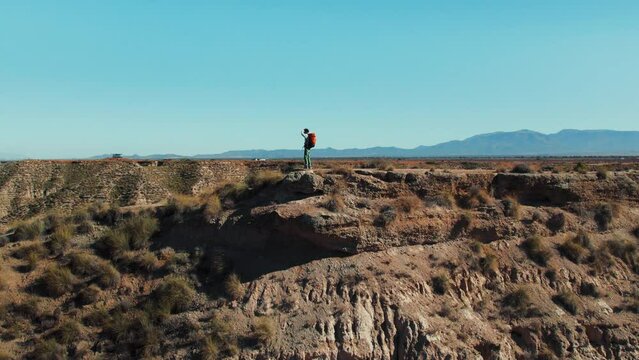 Man at the top of desert hill, taking in the breathtaking outdoor scenery, indulges his wanderlust. Explorer revels in the adventure of his journey, surrounded by peaceful mountain nature. 
