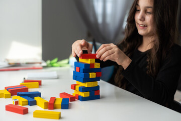 a little happy girl is playing the board game jenga at the table. Construction of a tower made of wooden cubes