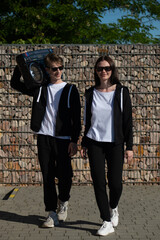 Fototapeta na wymiar A couple of teenagers on a walk with a boombox. Boy and girl on a date. Boy and girl in black tracksuits.