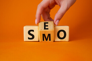 SEO vs SMO symbol. Businessman hand turns wooden cubes and changes the word SMO to SEO. Beautiful orange background. SEO vs SMO and business concept. Copy space