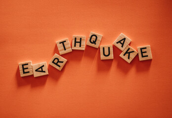 Obraz premium Inscription earthquake from vibration moves on background. Concept of earthquake, destruction and shifts of earth's crust. Wooden square blocks with letters are laid out on orange sheet. Slow motion