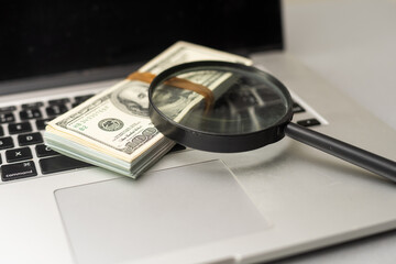 Magnifying glass and dollar bills on laptop. Search for financial income on Internet