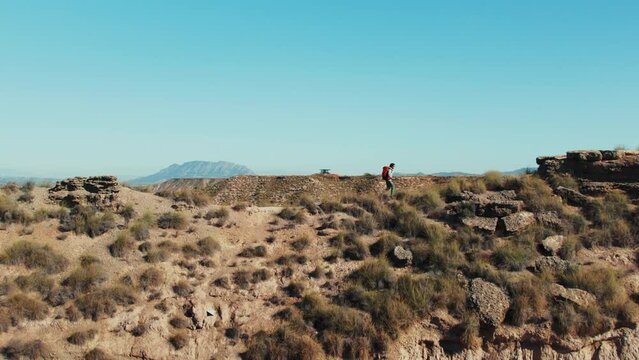 In the summer heat, man hikes in a desert hill, seeking an adventure among the stunning natural mountain scenery. Freedom lifestyle. Travel blog concept. Touristic adventure. 