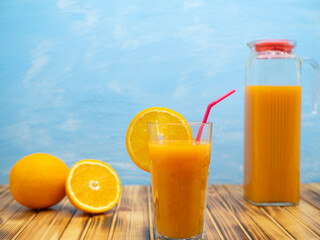 Glass and pitcher of orange juice on a wooden table on a blue background. Glass with orange cocktail.