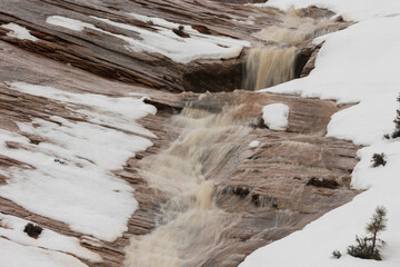 An ephemeral waterfall flowing between melting snow patches rushes down the layered red sandstone that makes up Zion Nat. park in Southern Utah, USA.