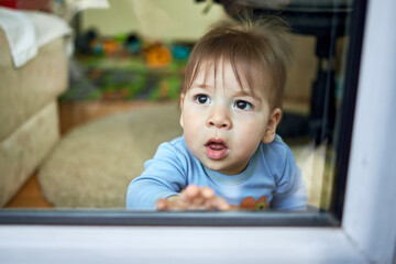 Cute little child, blond toddler boy sitting indoors looking through window