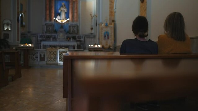 Two women are sitting on a bench in a church.