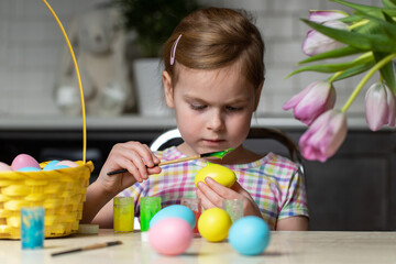 Little child painting Easter eggs sitting at table at home. Holiday craft