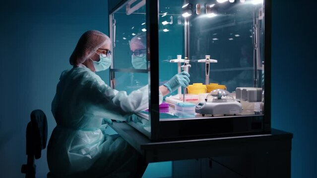 A female doctor in protective equipment putting in samples in tubes while working on a PCR cabinet. This work requires precision and careful and stady hands. High quality 4k footage 
