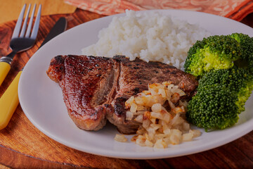 Beef steak with rice broccoli and fried onions on a white plate.