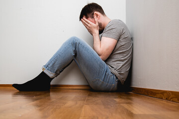 depressed man sitting in a corner of a room and covering his face