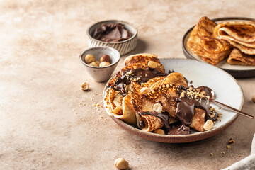 Crepes with chocolate and hazelnuts on beige background. Thin pancakes as delisious breakfast or dessert concept, Pancake day, Maslenitsa. Copy space