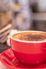 Hot chocolate served in red mug with cake in background